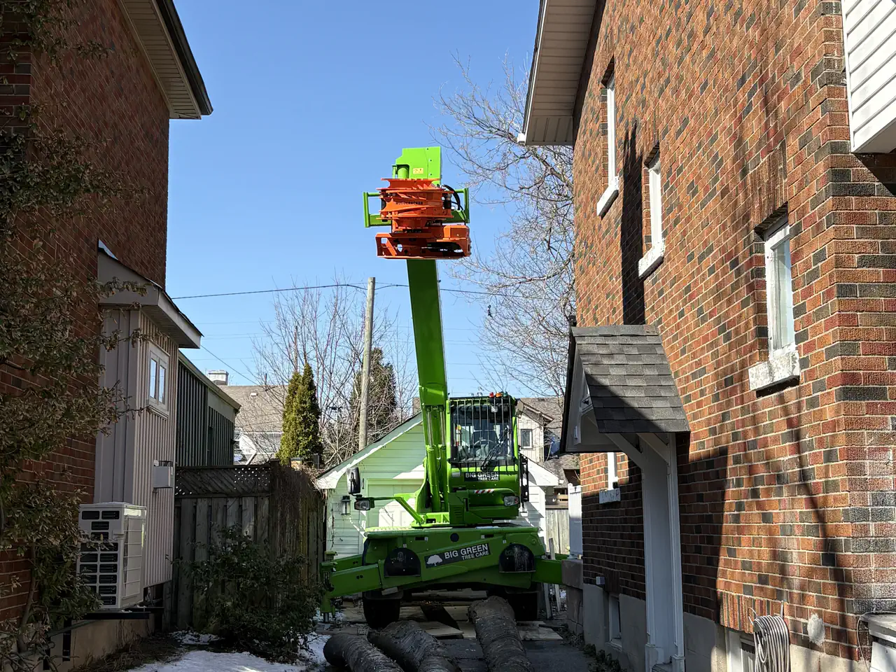 Grapplesaw reaching down a narrow side yard between two houses to remove a tree with no driveway access